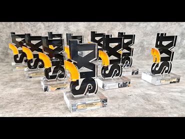 Βραβείο από πορτοκαλί και μαύρα ανάγλυφα γράμματα σε βάση από διάφανο plexiglass και label με εκτύπωση